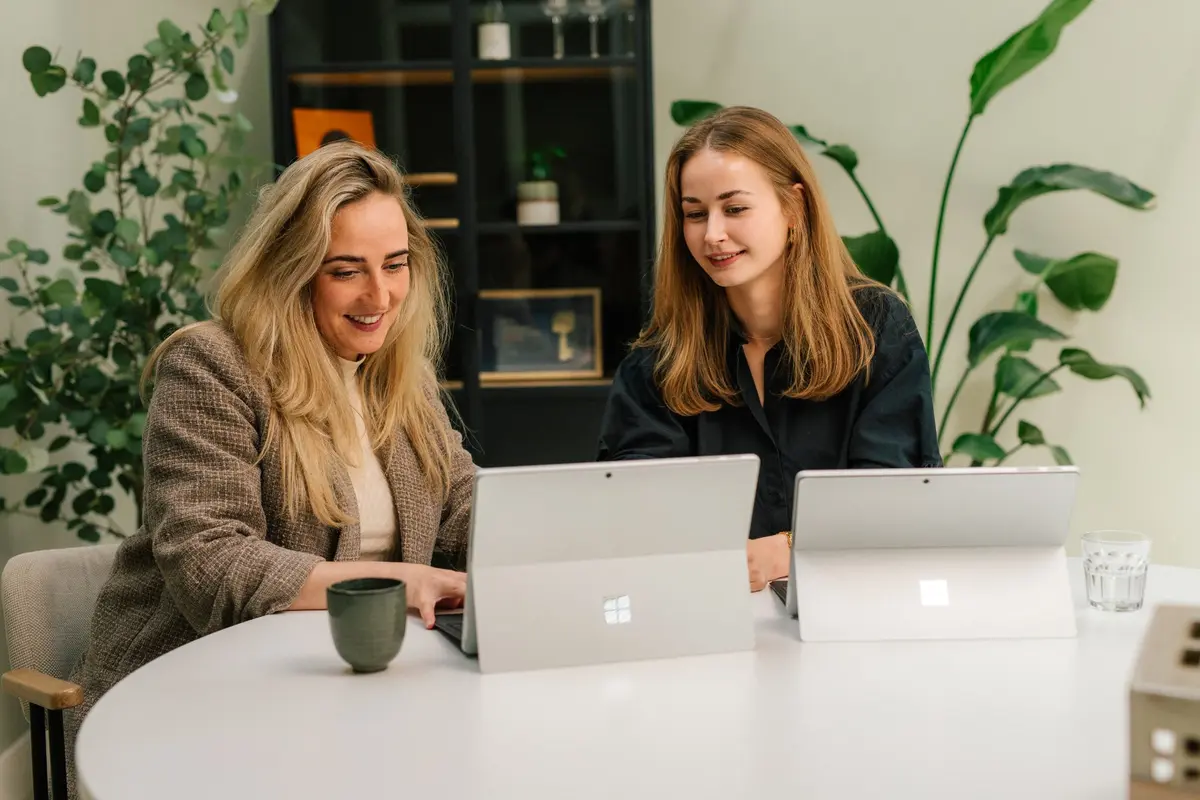 Twee collega's van Makelaardij Faber werken samen op hun laptop aan een ronde tafel