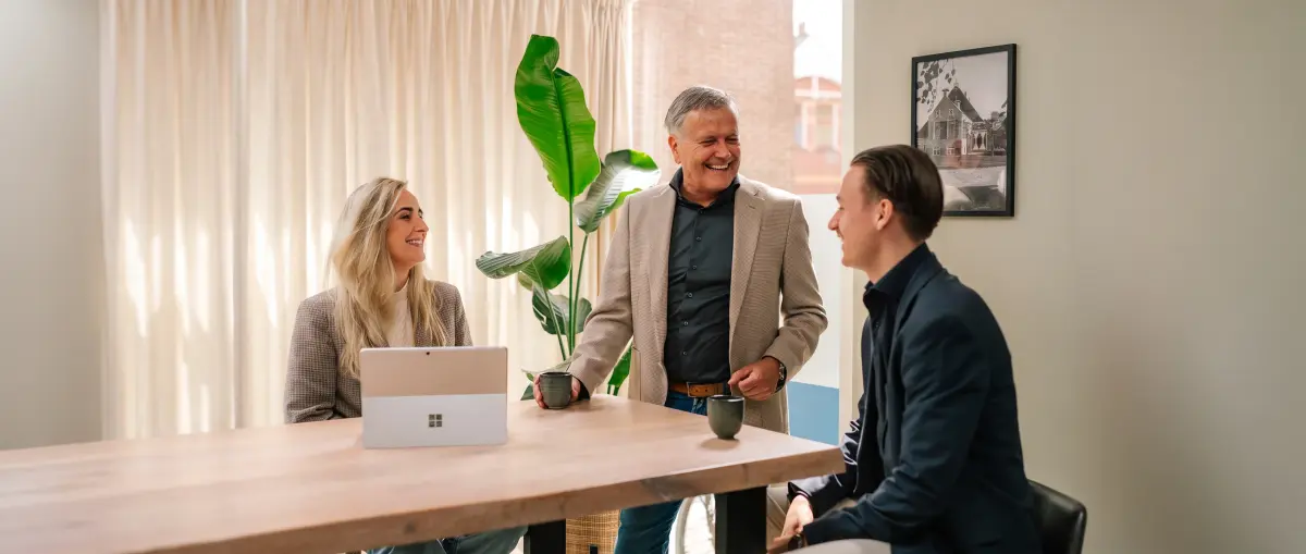 Drie collega's van Makelaardij Faber lachen samen aan de vergadertafel op kantoor
