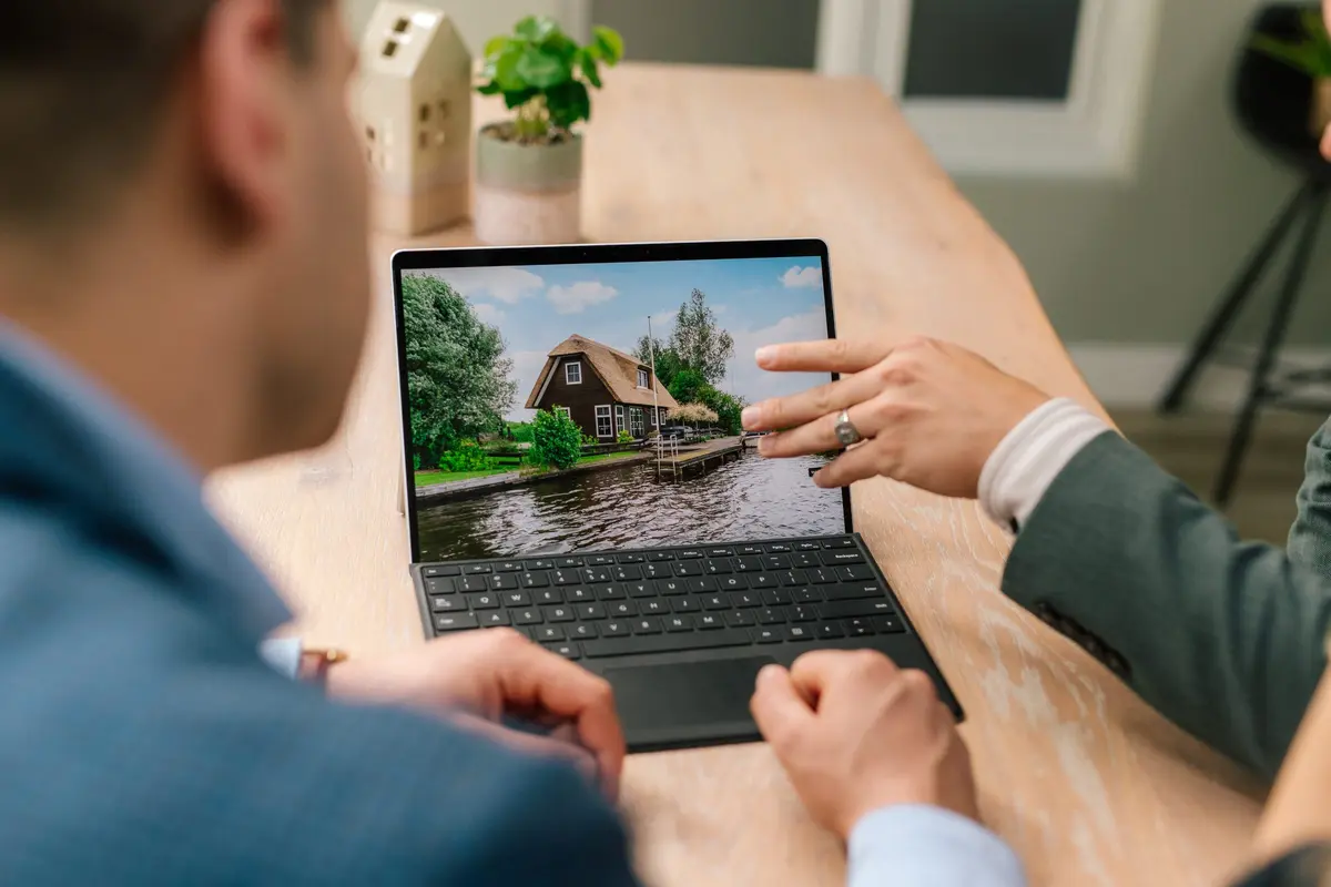 Een adviseur van Makelaardij Faber wijst op een laptop een woning aan het water aan